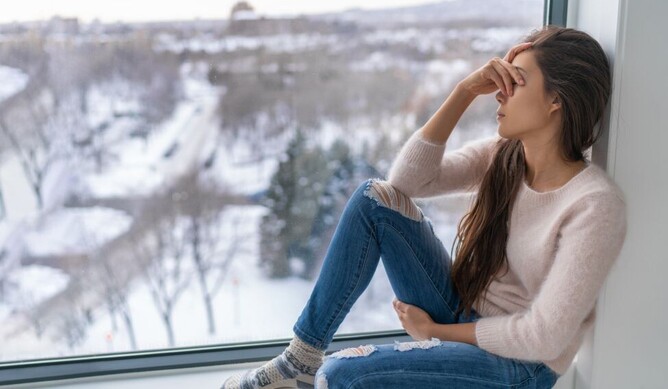 lady sitting in a window looking sad with the winter blues